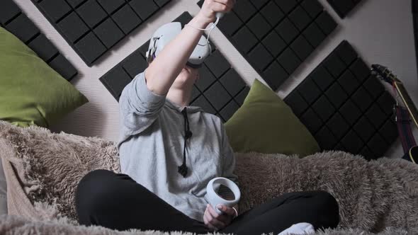 Young Woman Sitting on Sofa Playing Game Using VR Helmet Indoor at Home