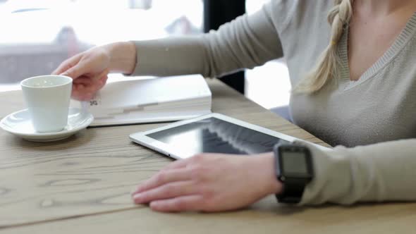 A business girl in a restaurant works with a tablet and drinks coffee.