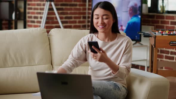 Joyful Asian Woman Texting Friend on Phone While Working Remotely