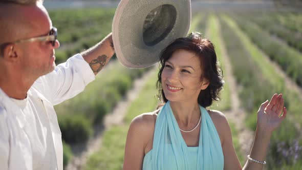 Beautiful Wife in Sunshine on Lavender Field with Husband Putting on Straw Hat in Slow Motion