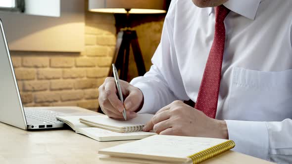 Businessman Sitting at the Table and Draws a Graph in a Notebook