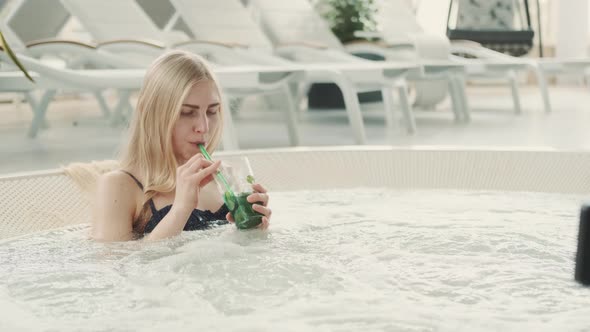 Medium Shot of Blonde Woman Resting in Jacuzzi with Soft Drink