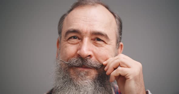 Close Up of Bearded Happy Senior Man Touching Moustache Isolated on Gray Background