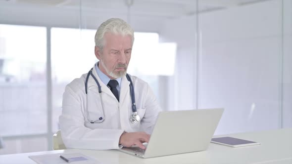 Focused Old Senior Doctor Working on Laptop