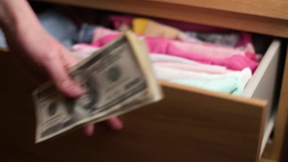 A woman takes money dollar hidden in children's things in a wardrobe