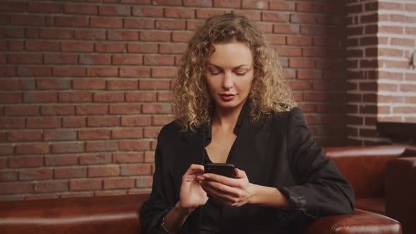 Handheld Shot of a Curly Caucasian Businesswoman Typing and Browsing on Her Smart Phone