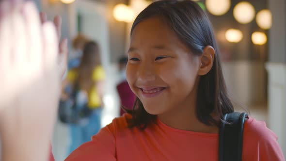 Close Up of Asian Preteen Schoolgirl Giving High Five To Classmate Standing in School Corridor