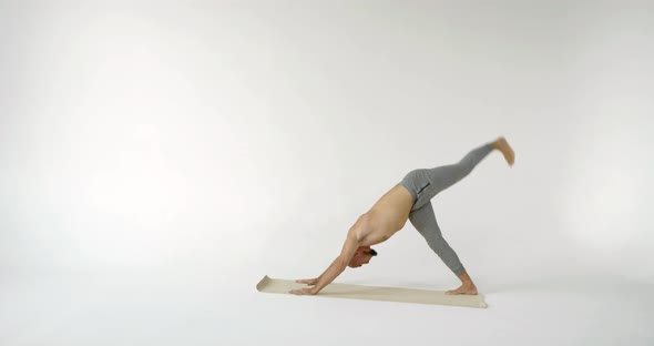 a Muscular Male Yogi Stands in a Pose Dog Muzzle Down and Rotates an Outstretched Leg