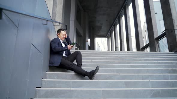 young asian depressed man sitting on the stairs outdoors street near office business