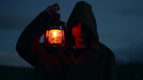 a Man of Caucasian Nationality in a Dark Green Raincoat with a Luminous Lantern the Evening Season