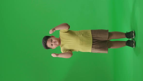 Full Body Of Happy Asian Little Boy Showing Thumbs Up Gesture While Standing In The Green Screen