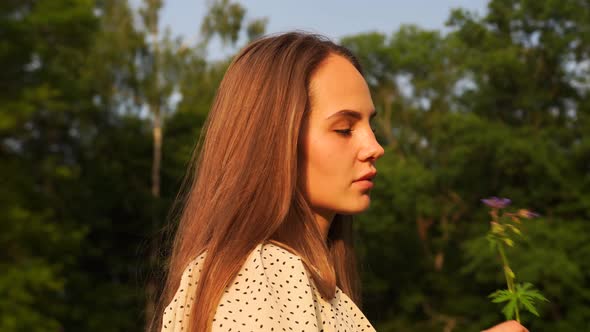 Woman in White Dress with Polka Dots Sniffing a Plucked Plant in the Forest