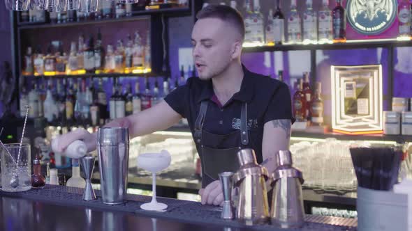 Cute Professional Barman Pouring Drink From Measuring Cup Into a Metal Shaker