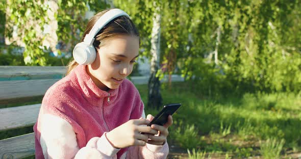 Ten Years Old Girl with Smartphone and in Headphones  She Chatting with Friends Outdoor