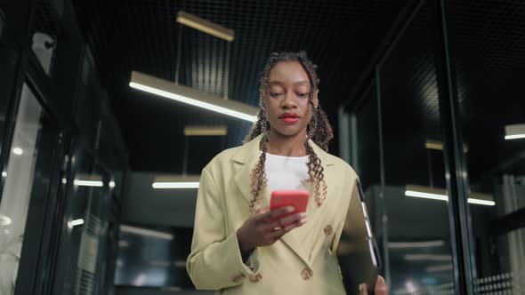 Portrait of a Black Business Woman Walking Down the Corridor of a Business Center and Typing a