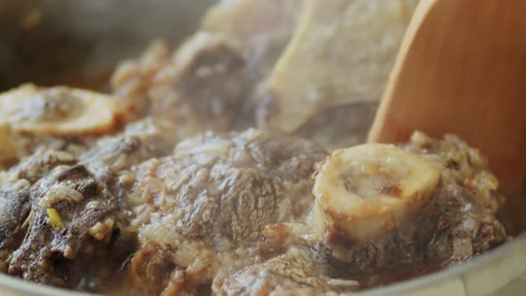 Person stirring hot veal shanks in frying pan