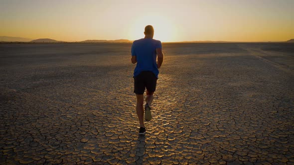 Athletic man working out with battle ropes on a dry lake at sunset