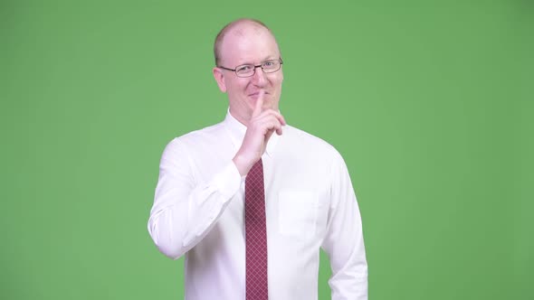 Happy Mature Bald Businessman with Finger on Lips