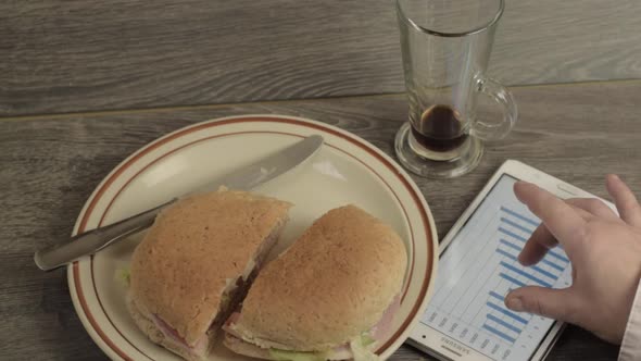 Busy person eating sandwich looking at a graph on a tablet