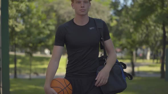 Portrait of Smiling Confident Sportsman Entering Outdoor Court with Sports Bag and Ball. Positive