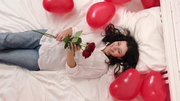 Excited Girl Falling on Bed Red Heart Shape Balloons with Bouquet of Flowers