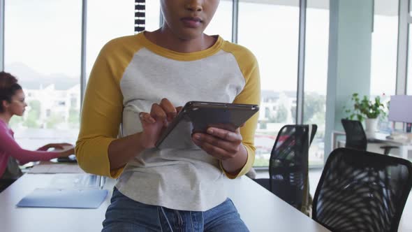 African american creative businesswoman using tablet in office, diverse colleagues in background