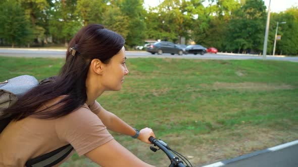 Young Woman Biking Near Busy Road with Cars