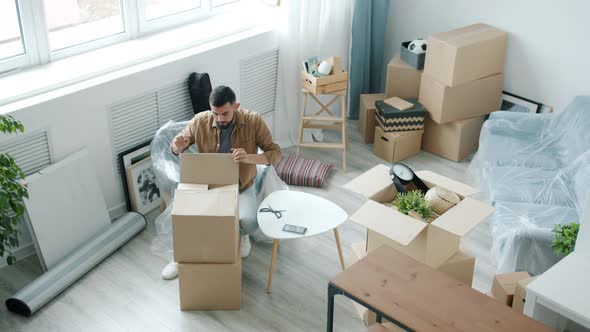 High Angle View of Arab Man Unpacking Containers with Personal Belongings Indoors in Light Room