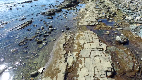 Tracking shot of a young man running on a rocky ocean beach shoreline