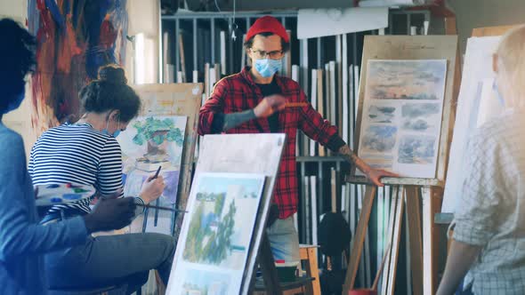 Male Painter in a Face Mask is Explaining Painting to Female Students