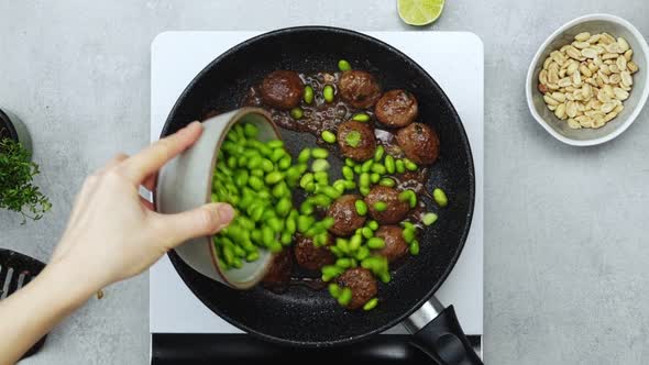 Woman adding green beans to meatballs