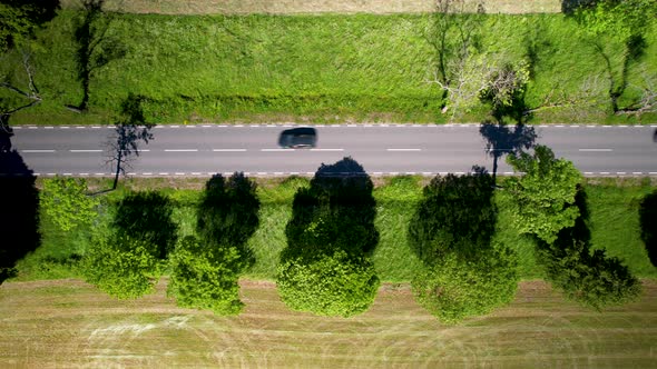 Aerial high angle shot of cars passing by on road between green fields on a bright sunny day. 4K.