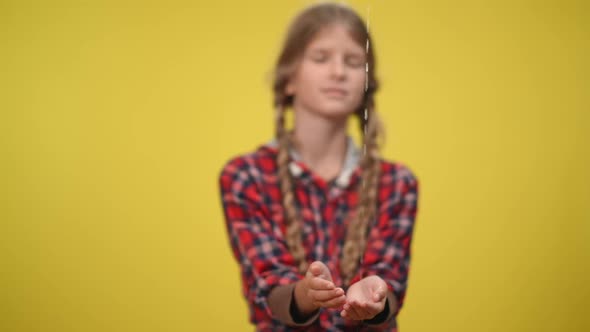 Water Pouring in Slow Motion on Hands of Blurred Teenage Caucasian Girl at Yellow Background