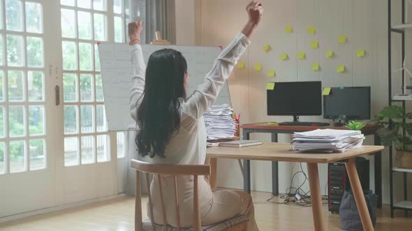 Back View Of Happy Asian Woman Celebrating Finishing Working With Documents At The Office