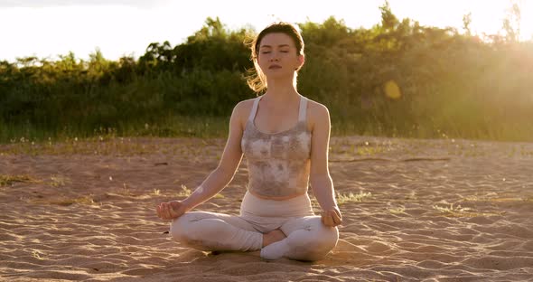 Woman practicing yoga outside in lotus pose on beach during sunset golden hour