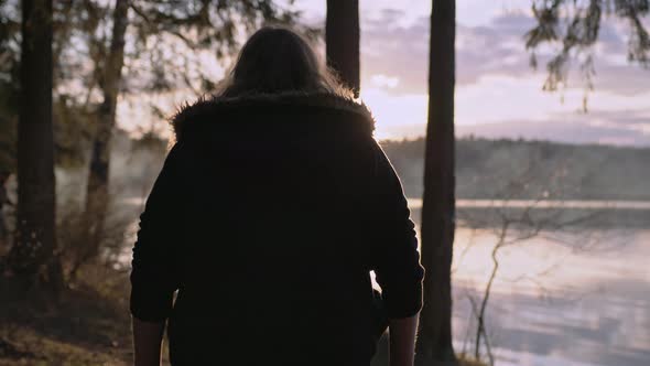 A Woman Walks Along the River Bank on a Cold Autumn Day in the Warm Autumn Sun