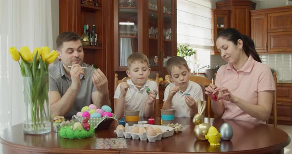 a Happy Family Sits at a Table and Paints Easter Eggs
