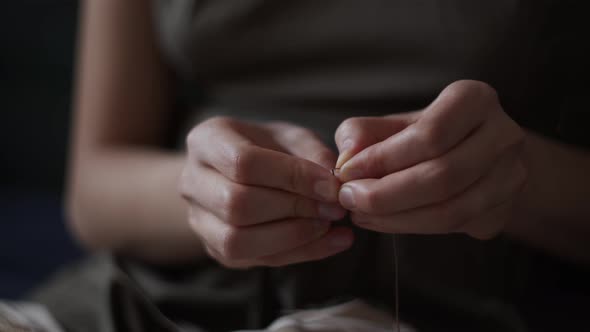 Close-up view of female hands inserting a thread into a needle hole for sewing. Handmade needlework.