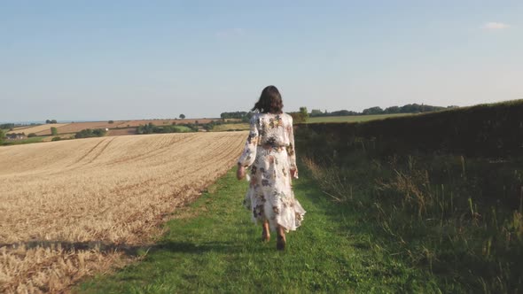Young woman in a long dress walks through a field and spins.