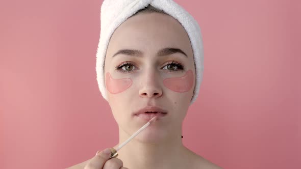 Plesant nude girl applying collagen eye masks on face in front of a mirror