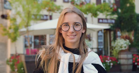 Happy Girl in Stylish Clothes and Glasses which Standing Near Cozy Street Cafe on Sunny Day 