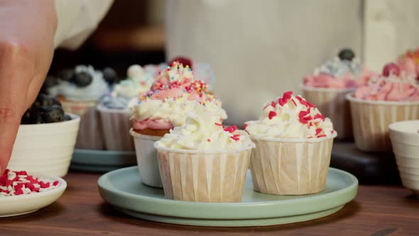 Woman Chef Decorating Cupcakes with Berries and Confetti Closeup