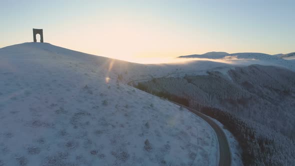 Aerial View of Susnet Over Snowy Misty Mountains with Slippery Mountain Winding Road