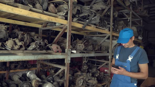 employee of auto disassembly, completes or checks car parts from tablet computer