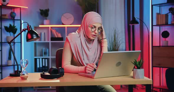 Muslim Woman in Hijab Sitting in front of Computer in Home Office and Working at Night