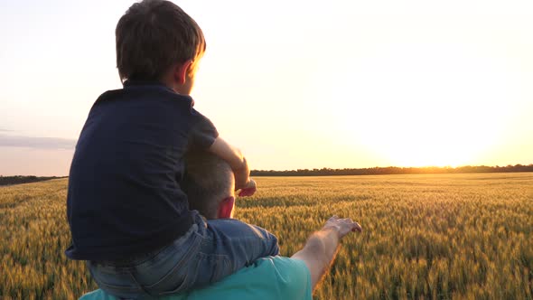 The Boy Is Sitting on His Father's Neck. Father and Son Point To the Horizon at Sunset. Happy Family