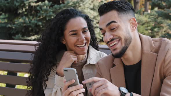 Bearded Guy with Attractive Girl in Autumn Park Sitting on Bench Cheerful Couple Interestedly Looks