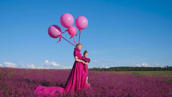 Fashionable Beautiful Woman in a Long Pink Dress with a Child Daughter Girl Stand on a Field with