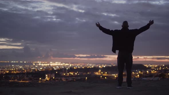 Man with Outstretched Arms Looking at City View at Sunset