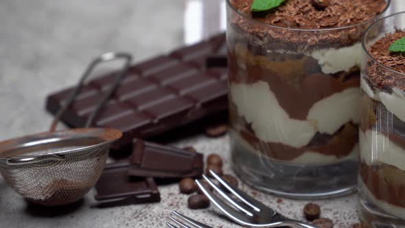 Two Portions Classic Tiramisu Dessert in a Glass and Chocolate Bar on Concrete Background